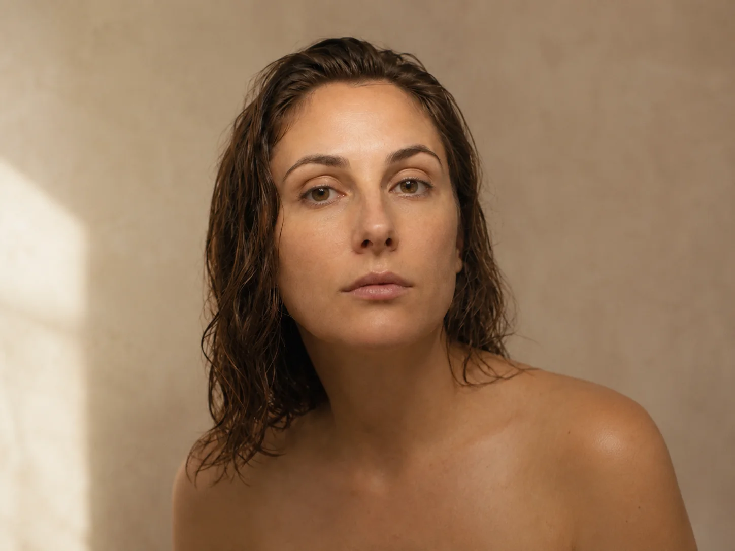 The same woman in the same position, this time in soft even daylight, looking calmly at her own skin.