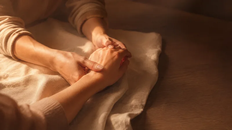 A consultant gently turning another woman’s hand to look at it, on cream linen.