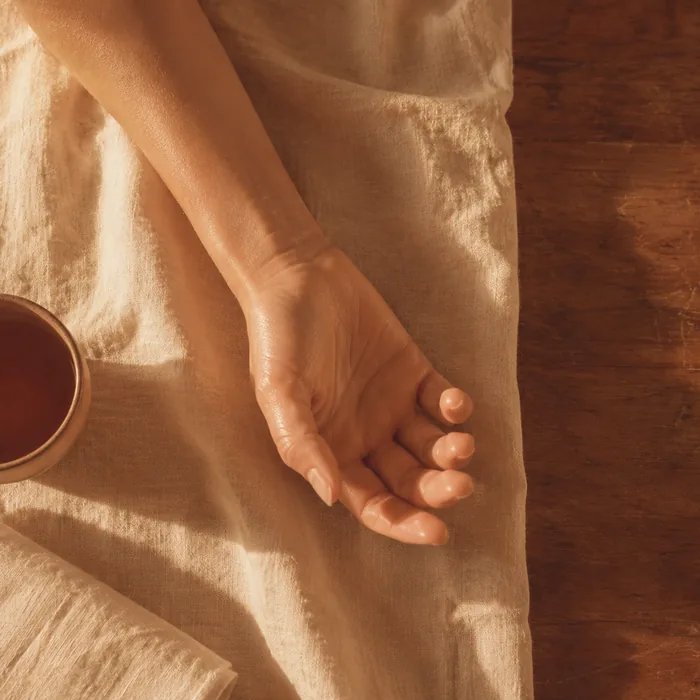 An open hand resting palm-up on cream linen beside a cup, seen from directly above.
